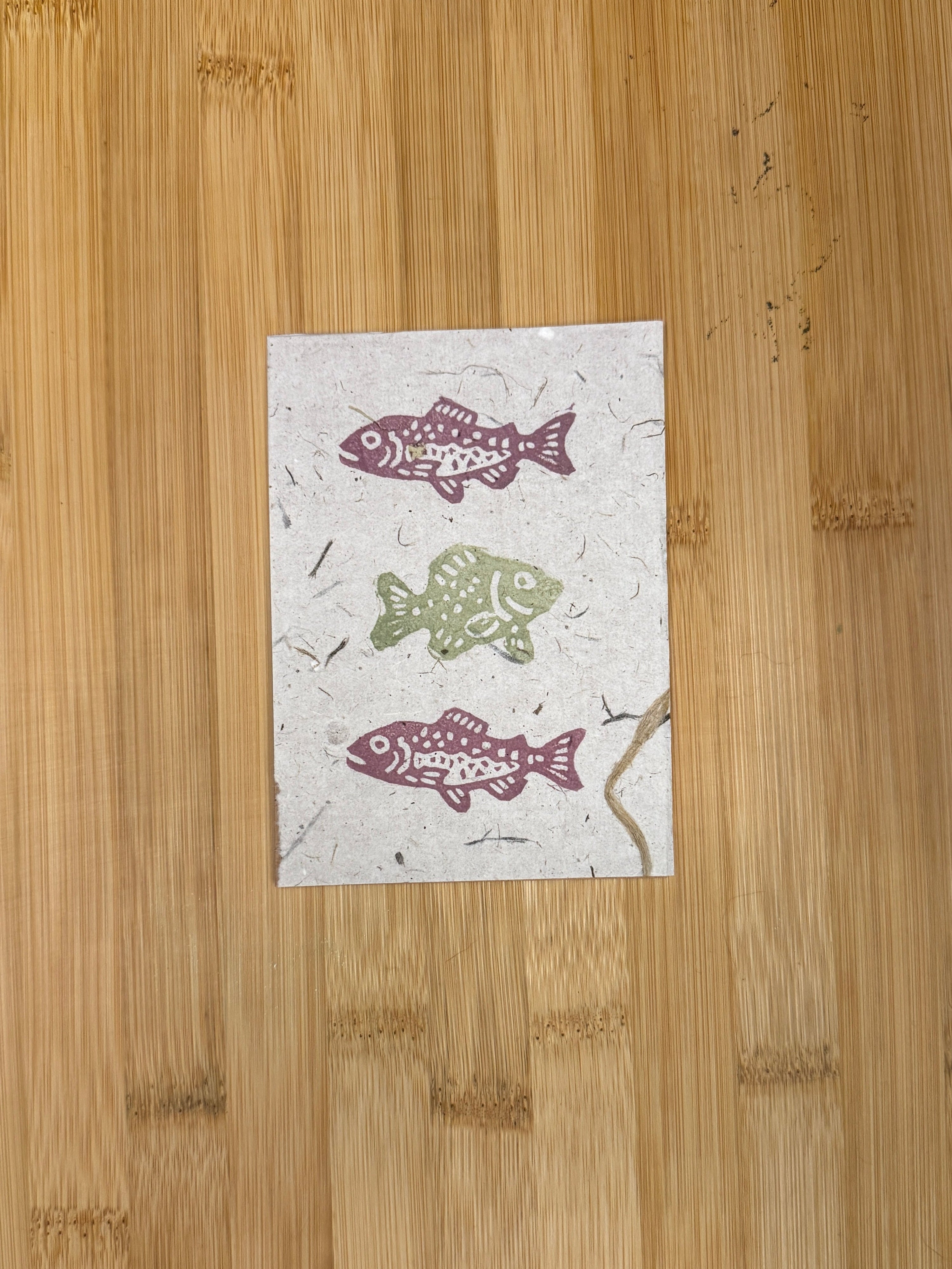 Three fish-shaped stamps on a piece of paper placed on a wooden  board.