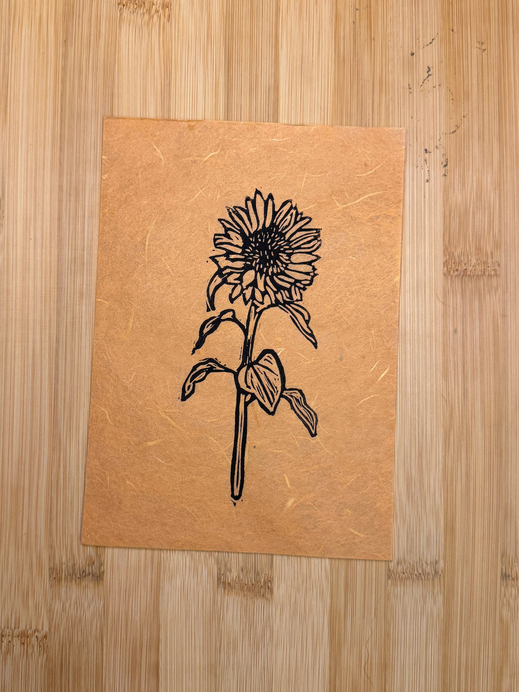 Black ink sunflower print on cantaloupe colored paper on wooden background.
