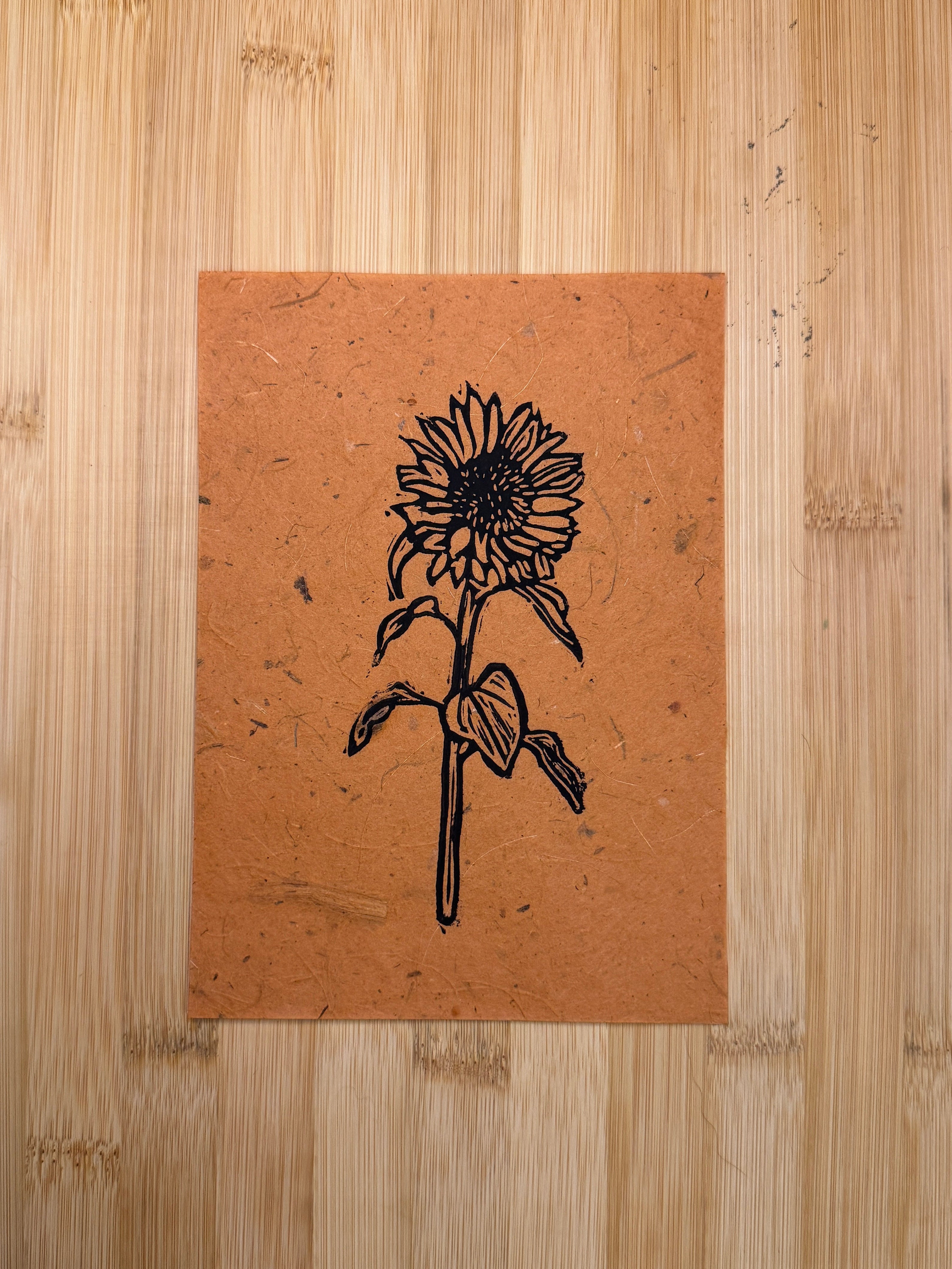 Black sunflower print on rust colored paper with wooden background.