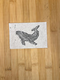 Wooden cutting board with a printed design of a whale on a white paper.