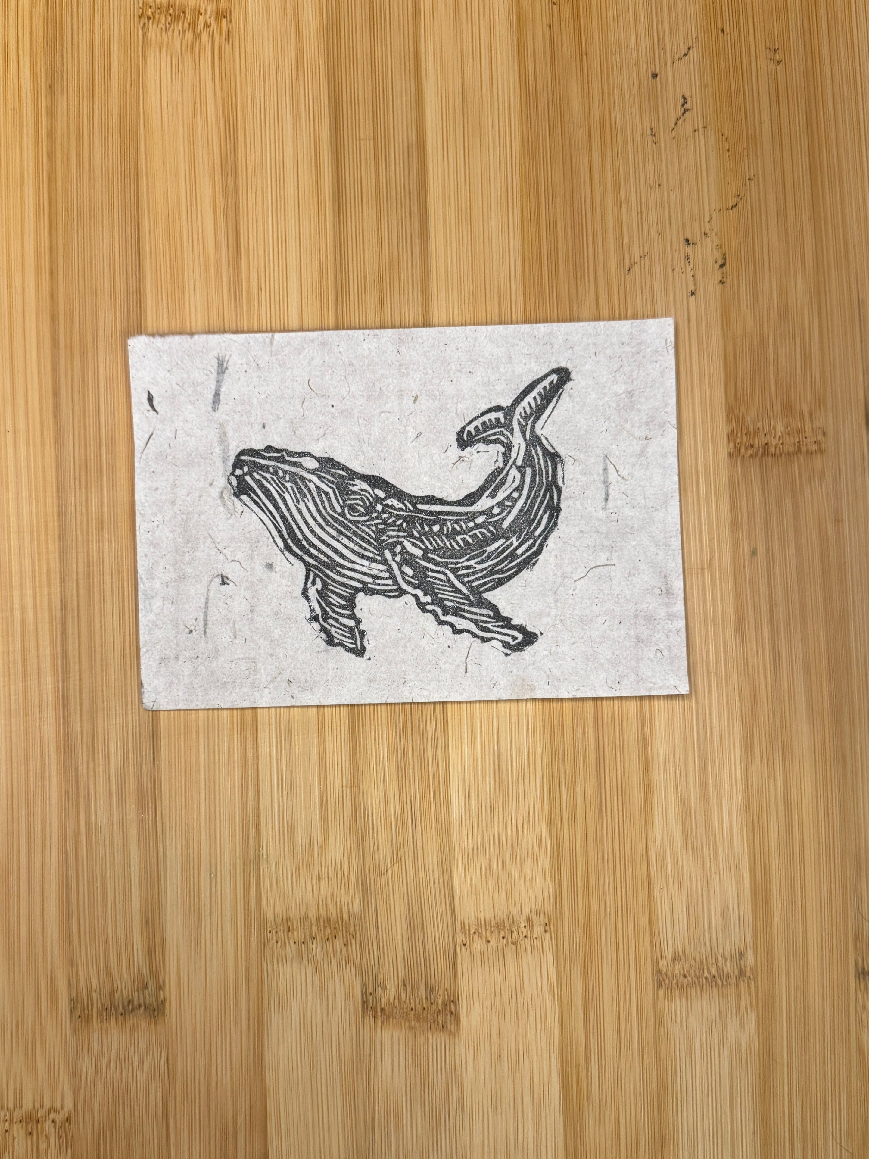 Wooden cutting board with a printed design of a whale on a white paper.